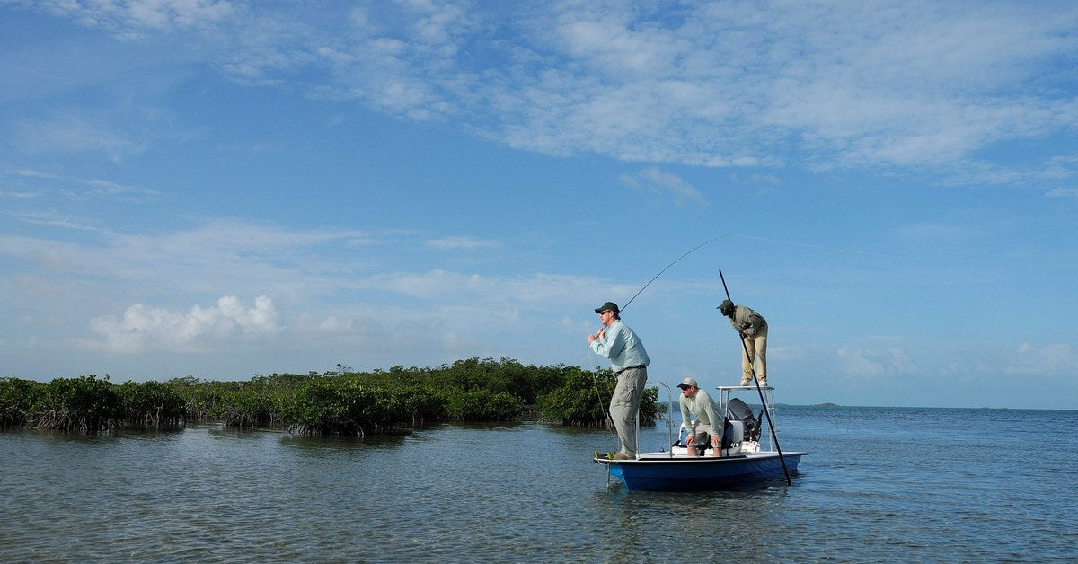 Angler hooked up from a flats skiff poled along a Bahamian mangrove edge