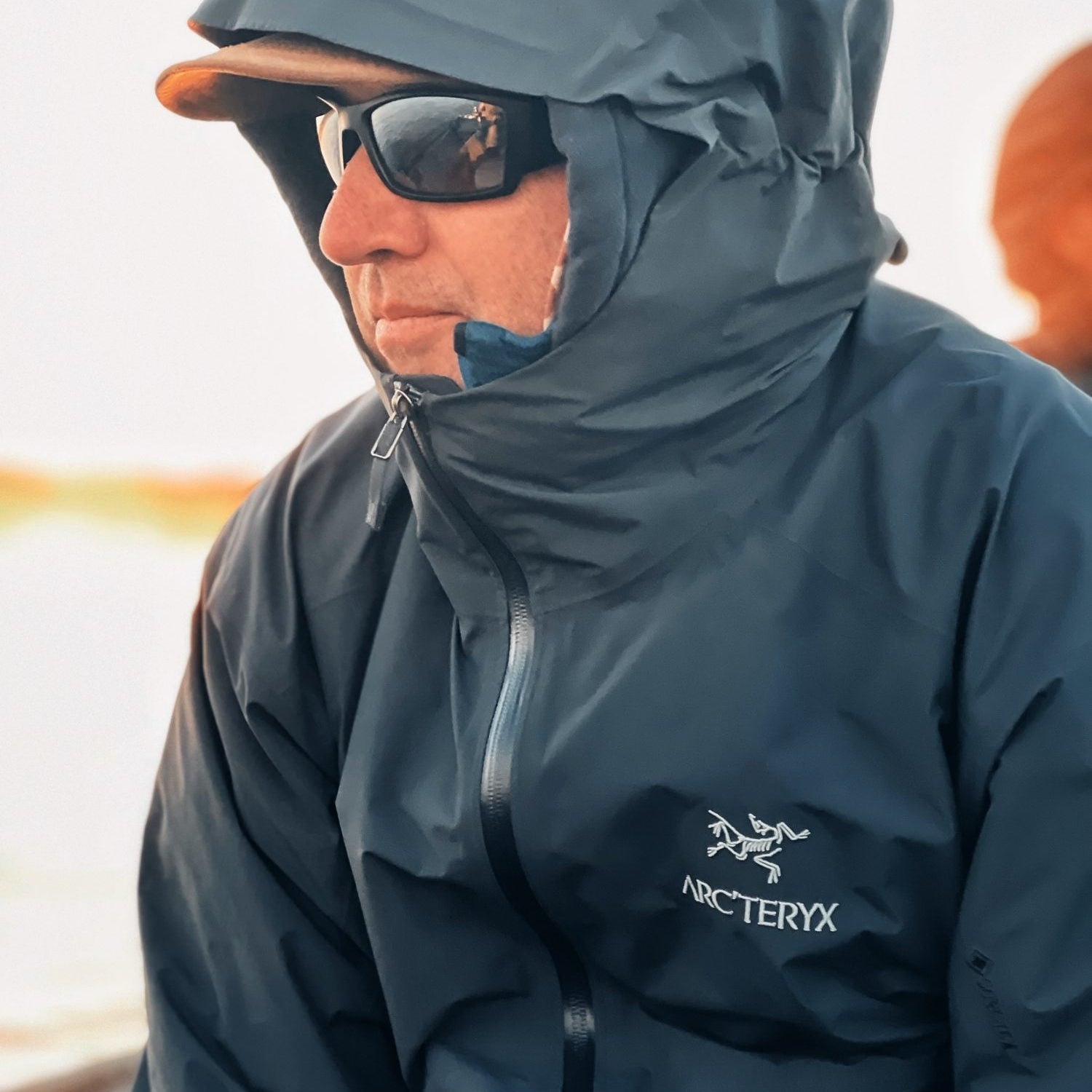 Angler in a hooded blue-gray Arc'teryx GORE-TEX shell jacket with the hood up and the Arc'teryx logo on the chest