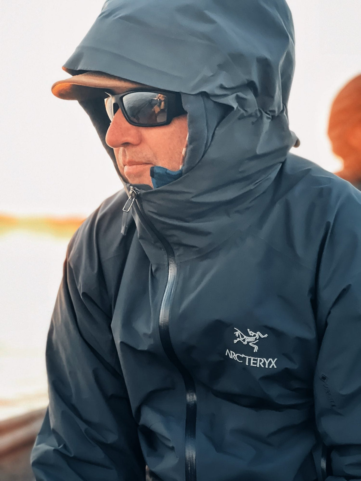 Angler in a hooded blue-gray Arc'teryx GORE-TEX shell jacket with the hood up and the Arc'teryx logo on the chest