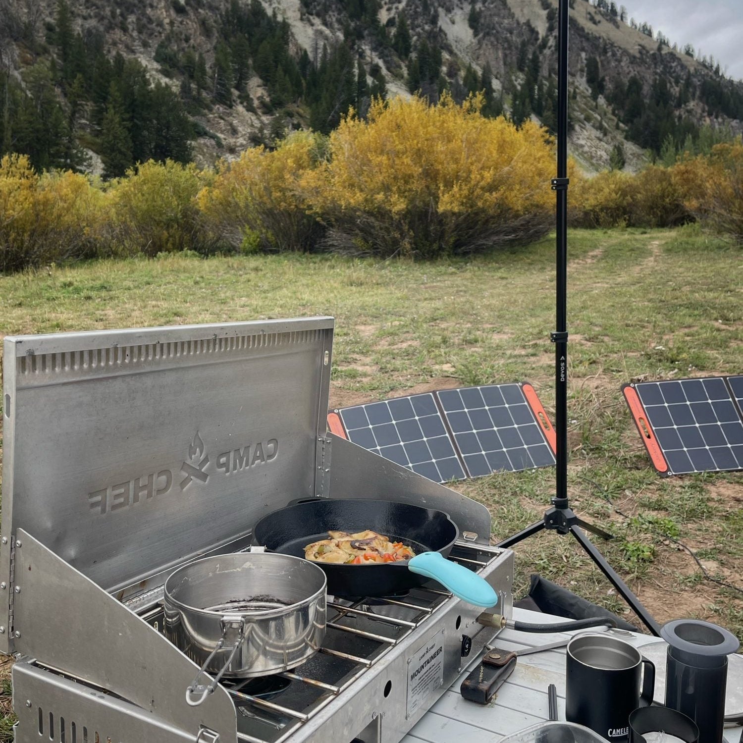 Jackery SolarSaga folding solar panels set in a meadow behind a Camp Chef Mountaineer stove and cast iron skillet