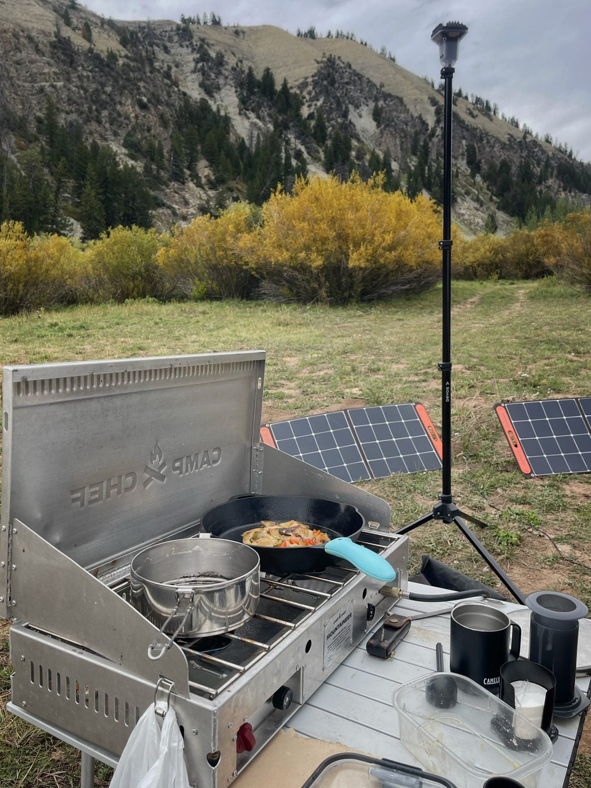 Jackery SolarSaga folding solar panels set in a meadow behind a Camp Chef Mountaineer stove and cast iron skillet