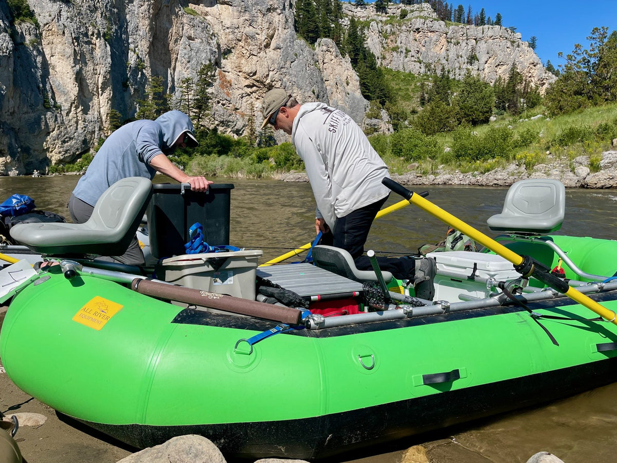 Two anglers rigging a green raft on a river, with the Camp Chef Sherpa Table Organizer packed for the day