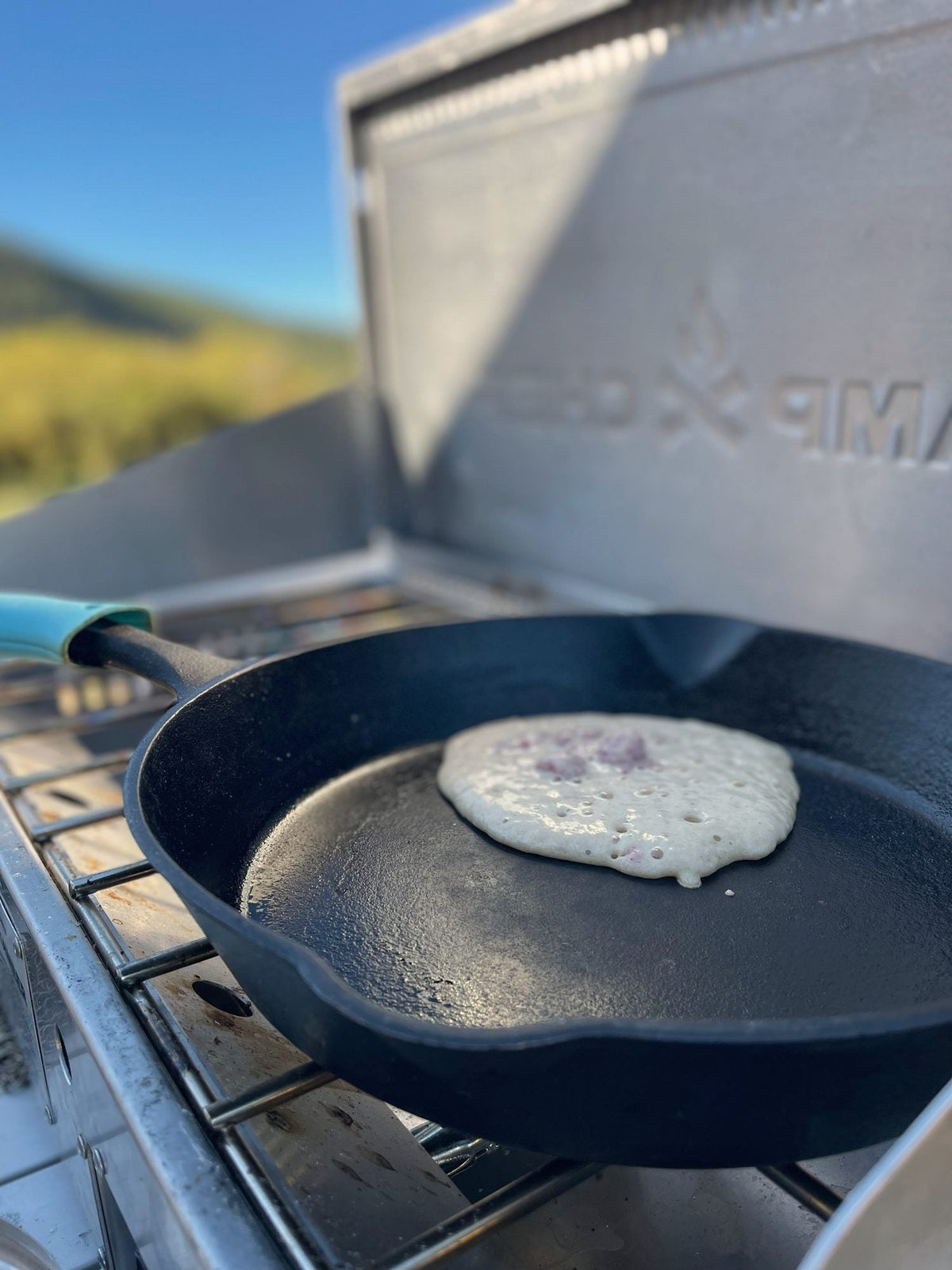 Camp Chef cast iron skillet with a pancake cooking on a Camp Chef Mountaineer stove at camp