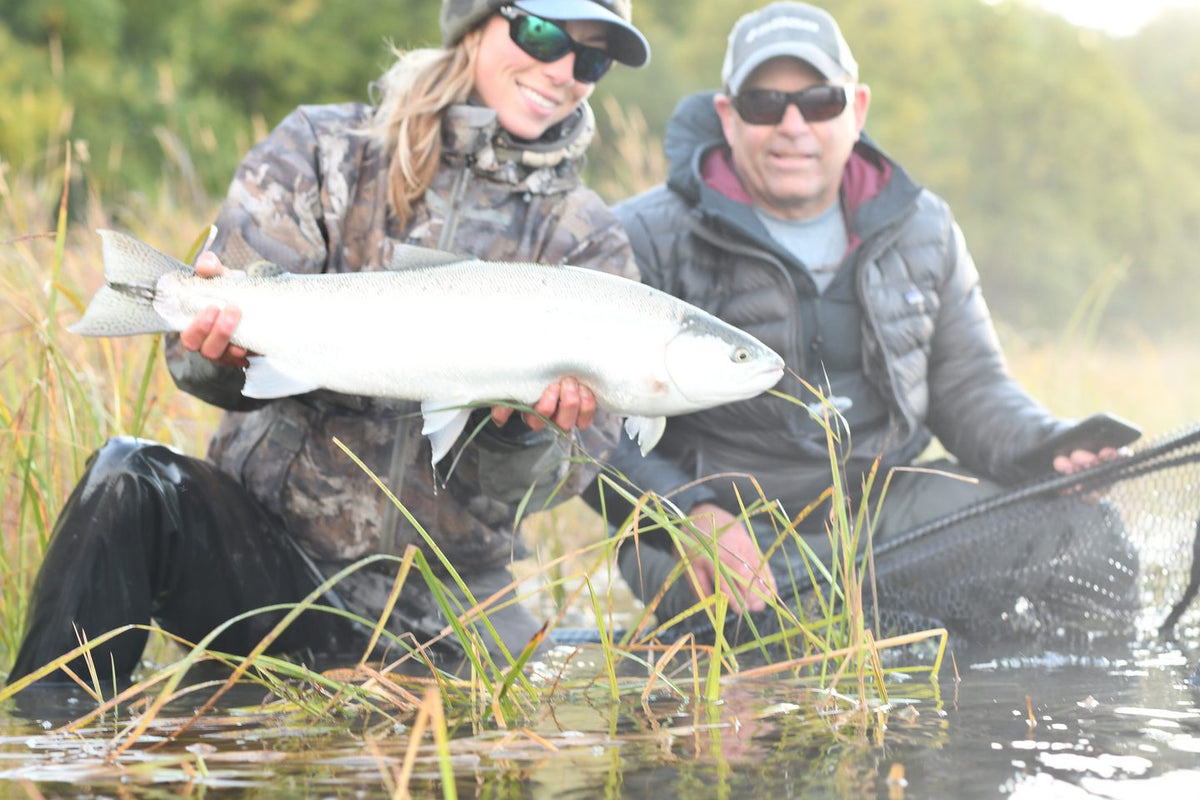 Two anglers holding a fresh chrome salmon on a Bristol Bay river in Alaska