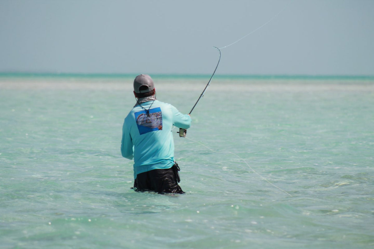 Angler wading a turquoise saltwater flat and casting for tarpon in Belize