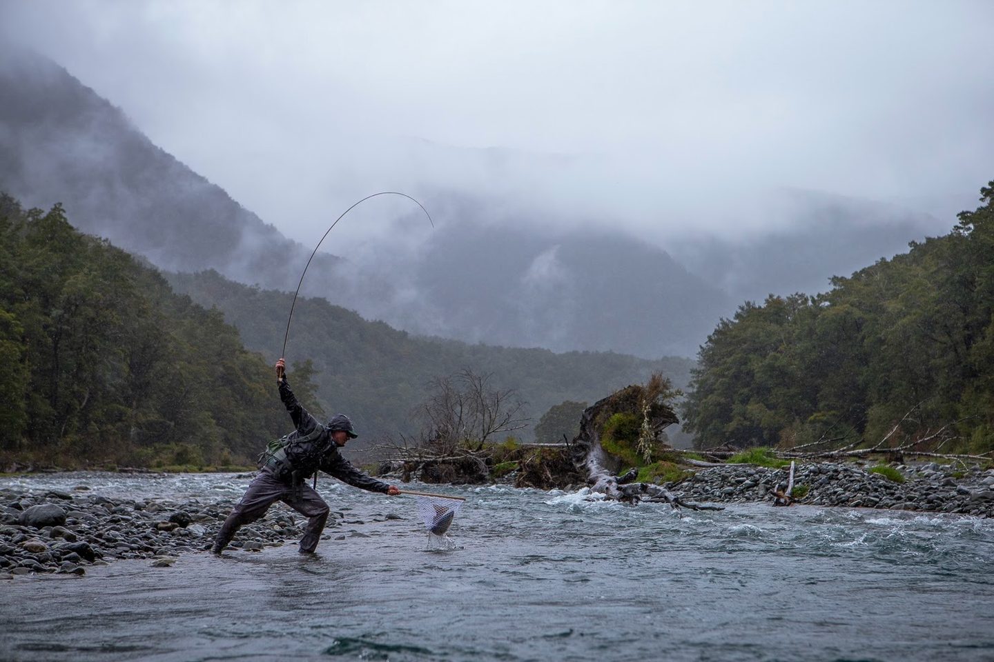 Angler fighting a fish on a misty mountain river