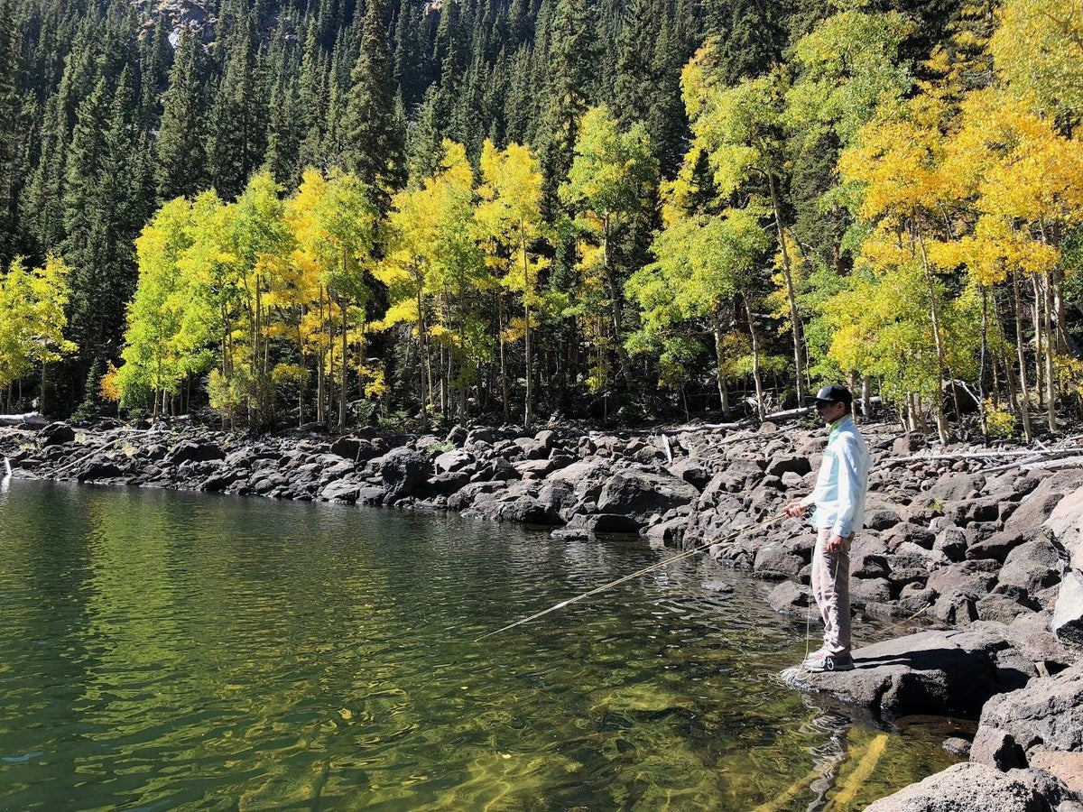 Angler fishing from a rocky lakeshore lined with golden aspens
