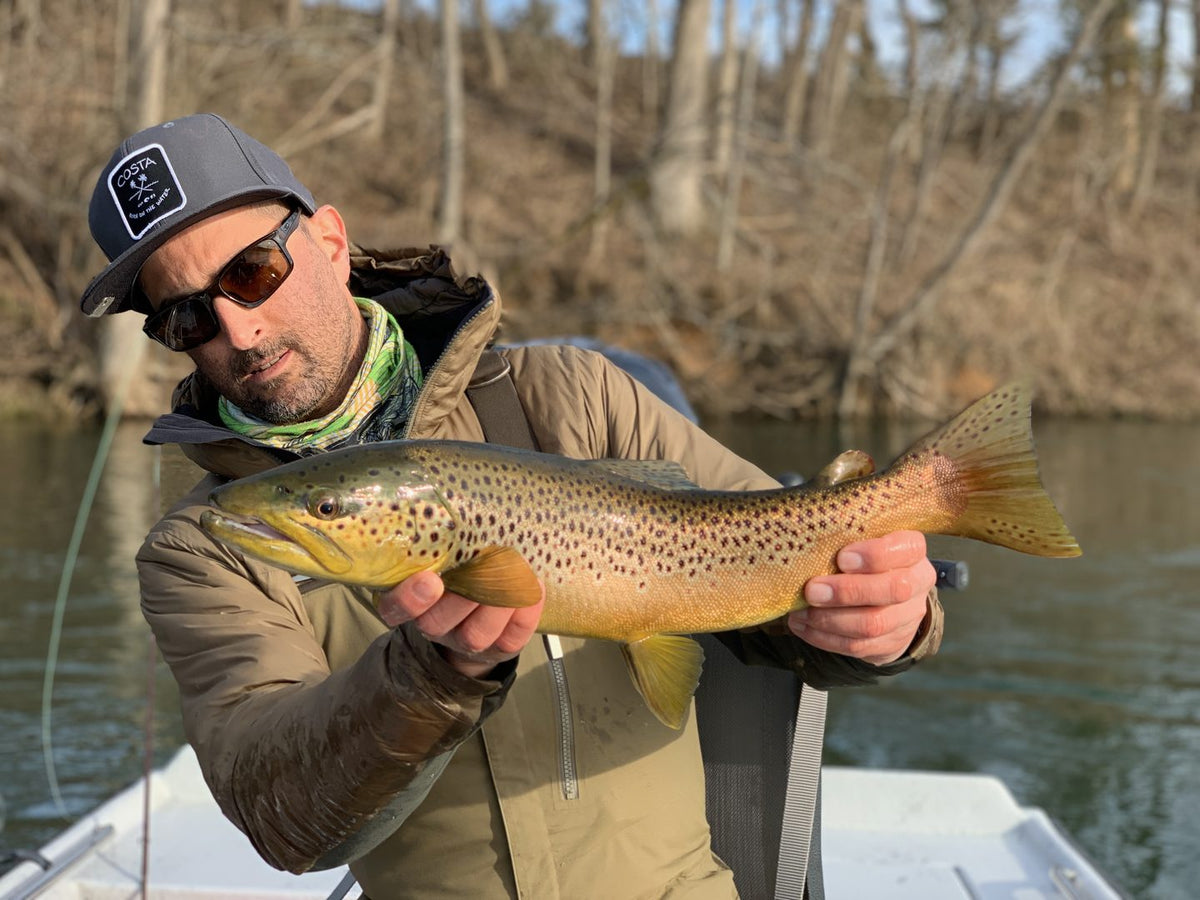 Angler holding a big brown trout on a river in fall