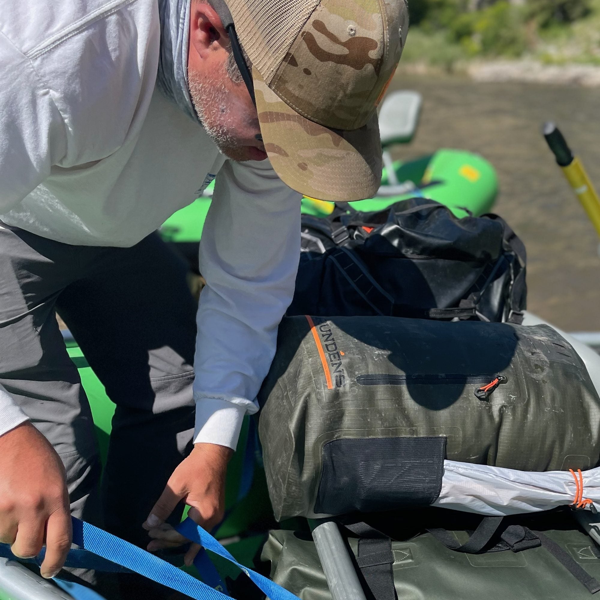 Grundens Wayward roll top backpack strapped down on a raft frame while an angler tightens a blue strap