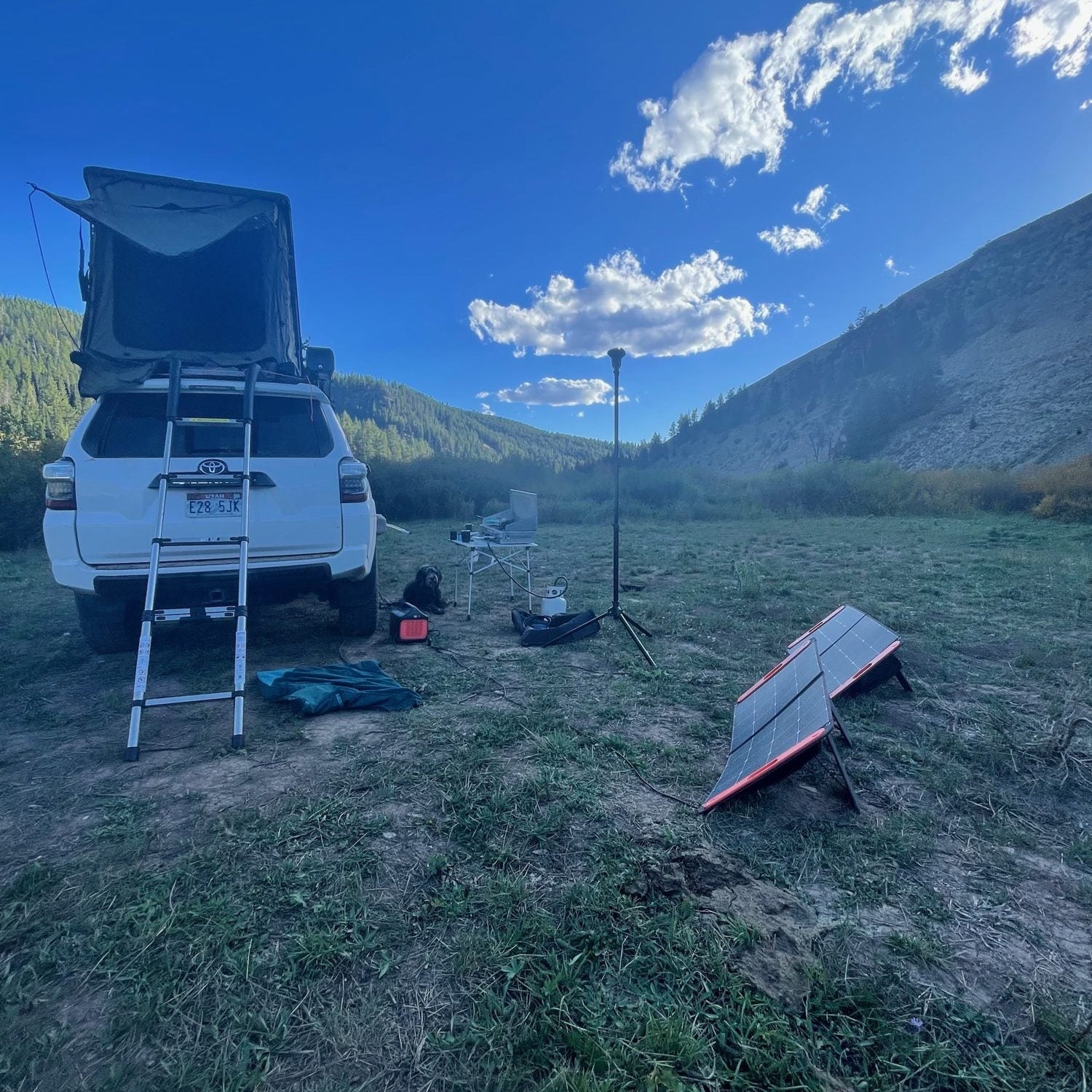 Jackery Explorer portable power station beside folding solar panels at a rooftop tent camp with a dog