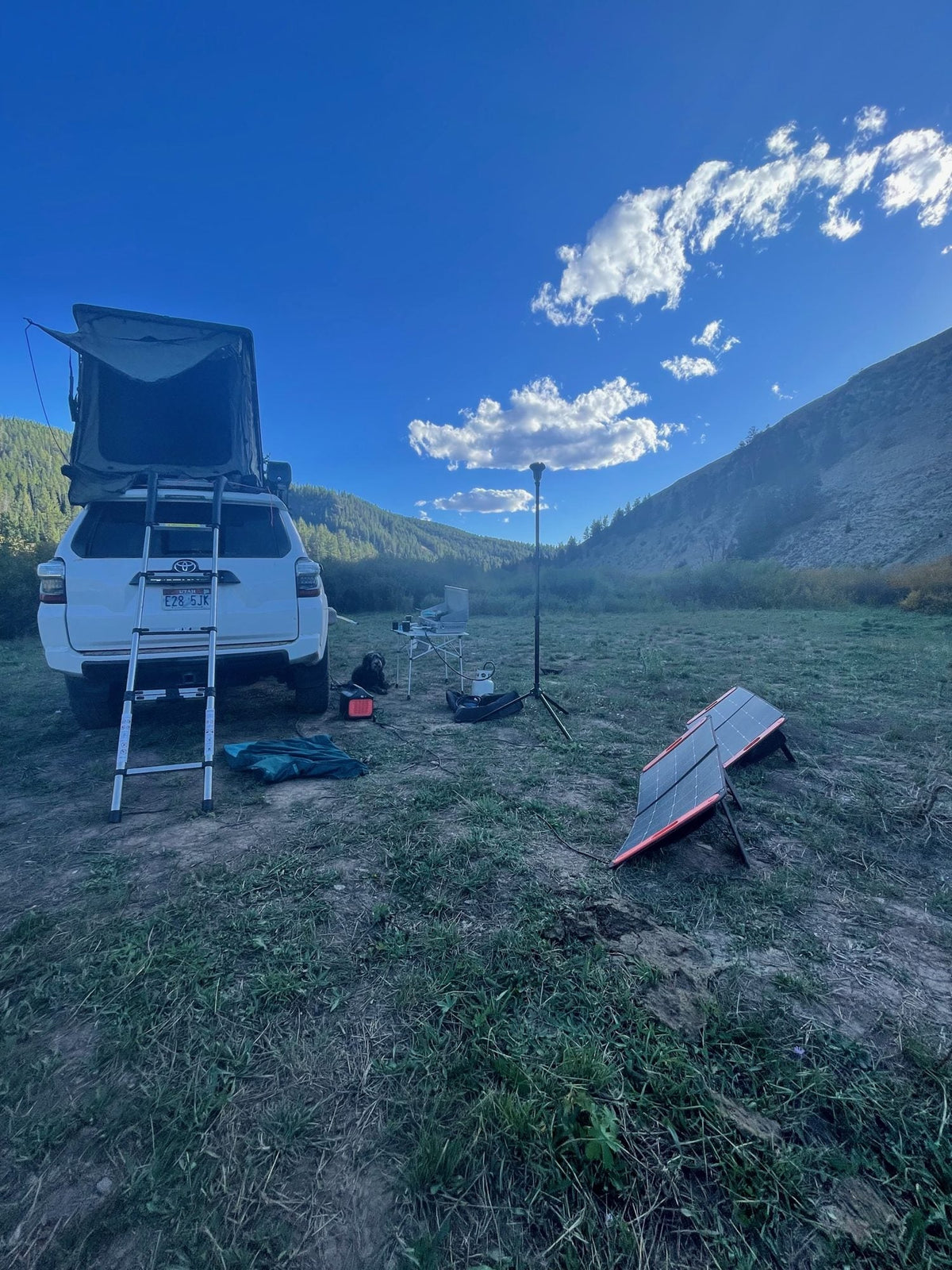 Jackery Explorer portable power station beside folding solar panels at a rooftop tent camp with a dog