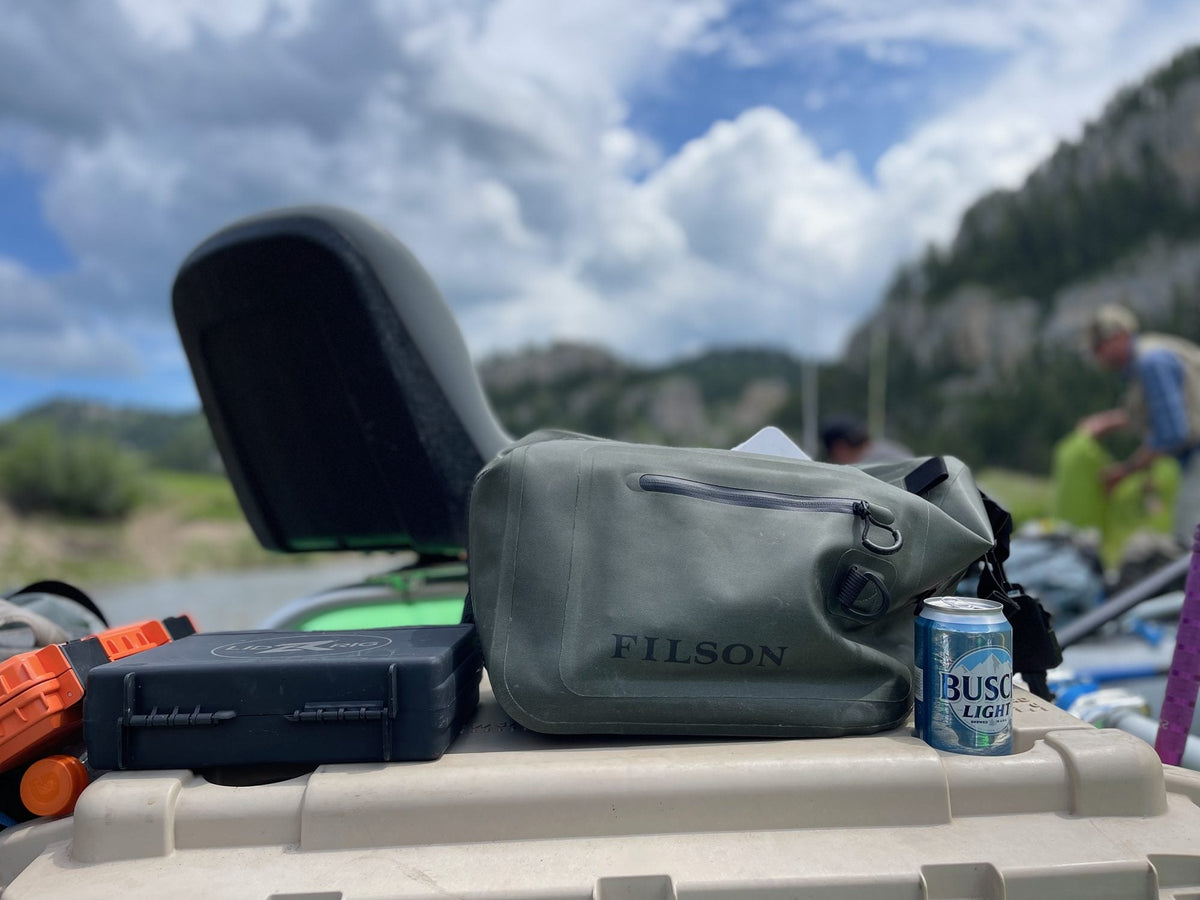 Black Lid Rig Mag Box Pro sitting on a cooler lid next to a Filson dry sling pack on a raft
