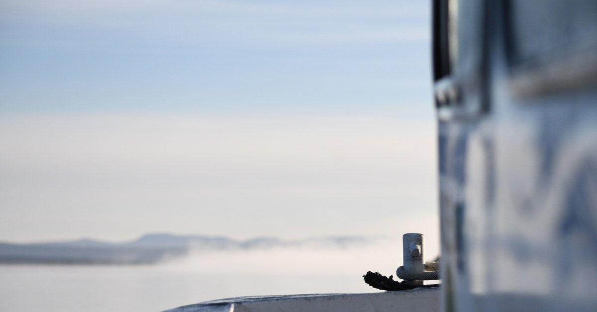 The rail of a boat on flat Alaskan water at dawn, low mist over a distant shoreline
