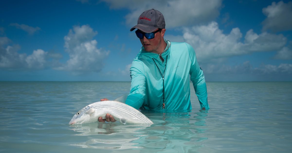 Angler in a Frontiers cap holding a bonefish at the surface on a sunlit tropical flat