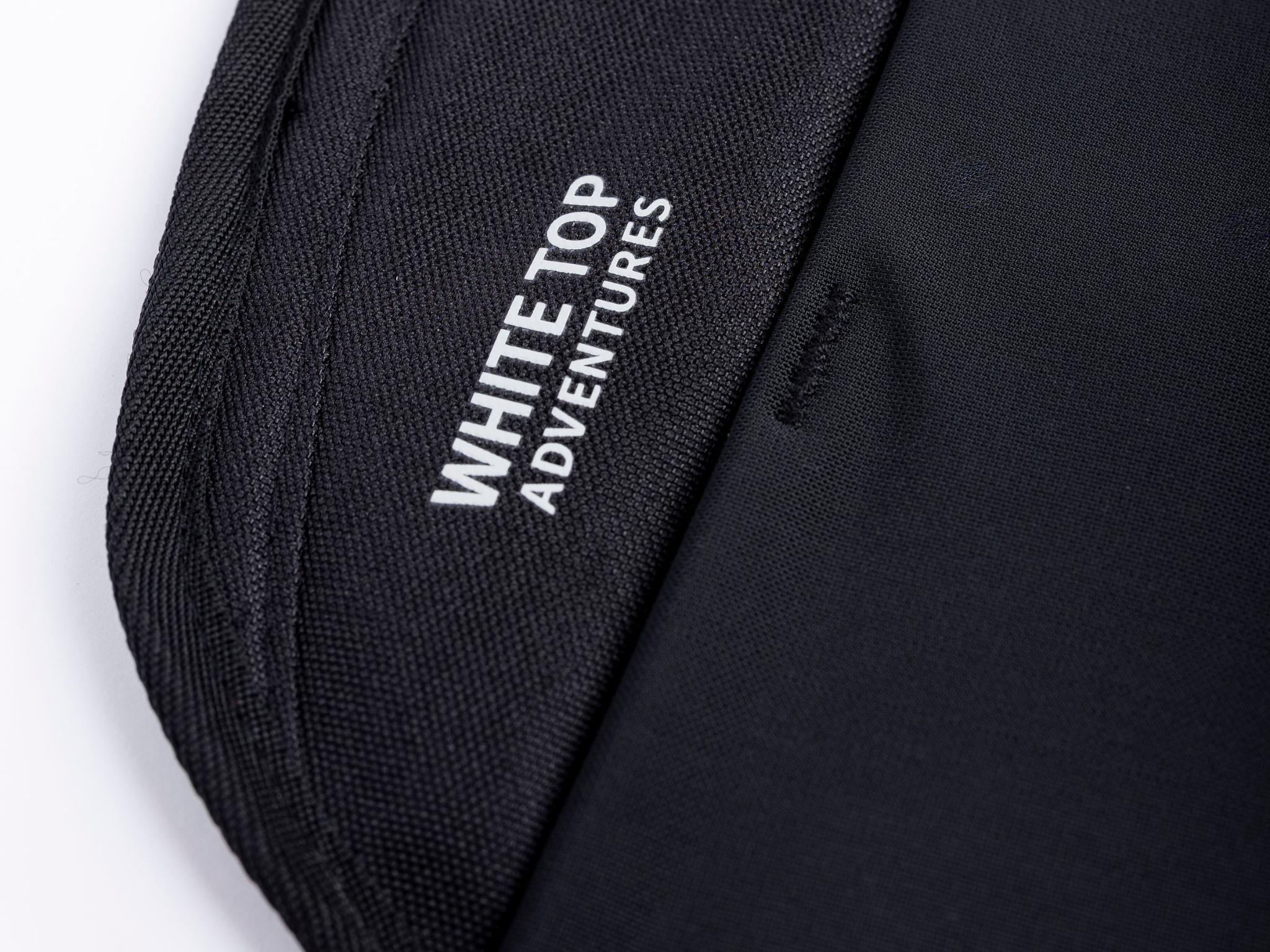 Black storage panel with label reading 'WHITE ADVENTURES' on woven fabric