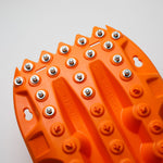 Orange metal-tooth traction board close-up with steel studs