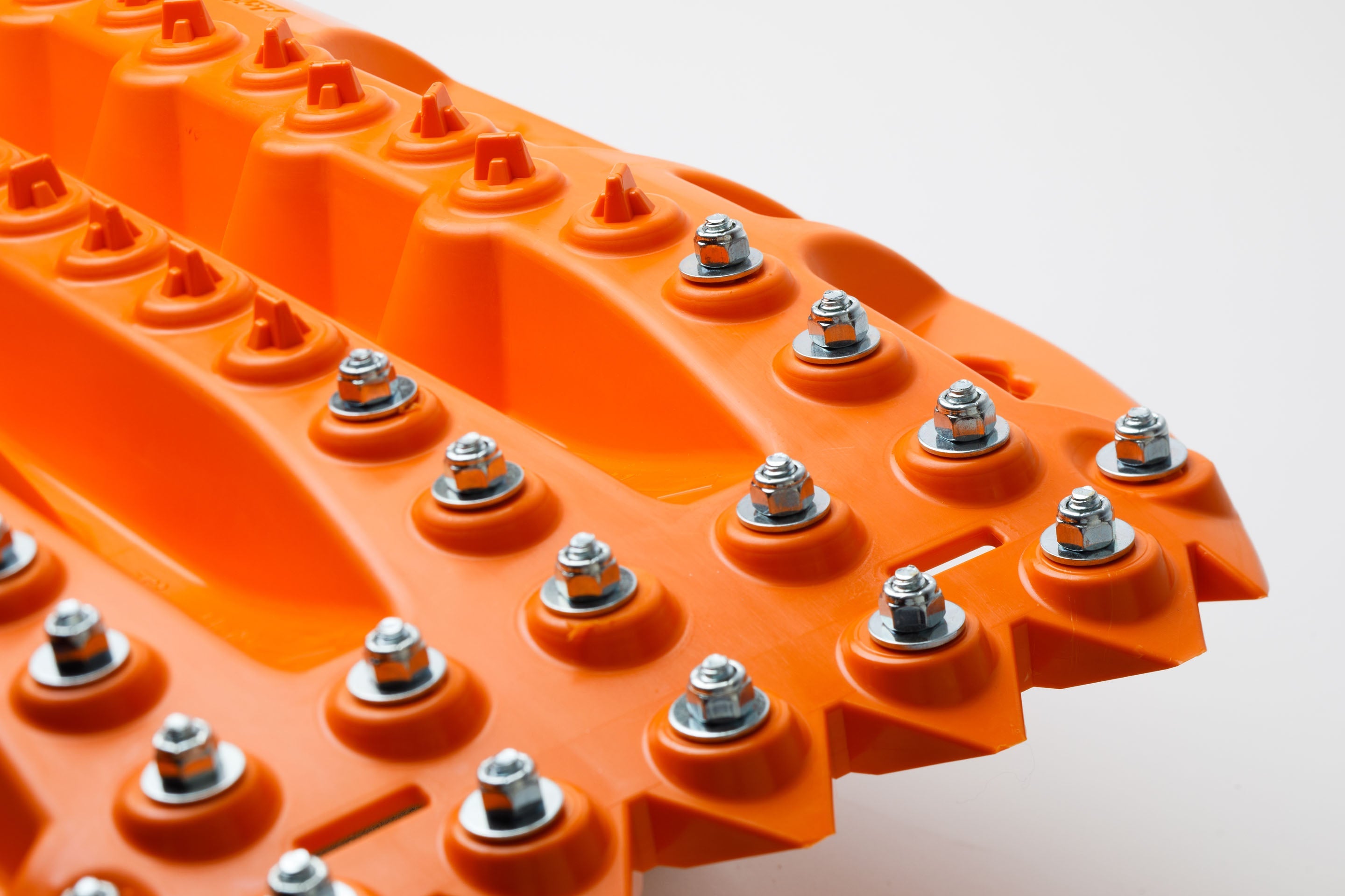 Orange traction board close-up with raised ridges and steel bolts