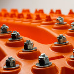 Orange recovery traction mat with metal stud bolts on raised ridges
