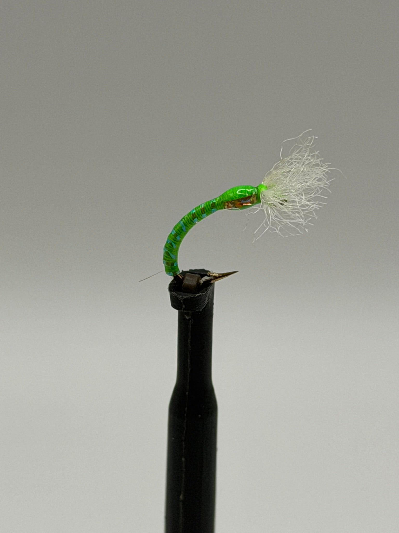 Chironomid buzzer fly lure on black stem, bright green body, white feather tail, barbed hook