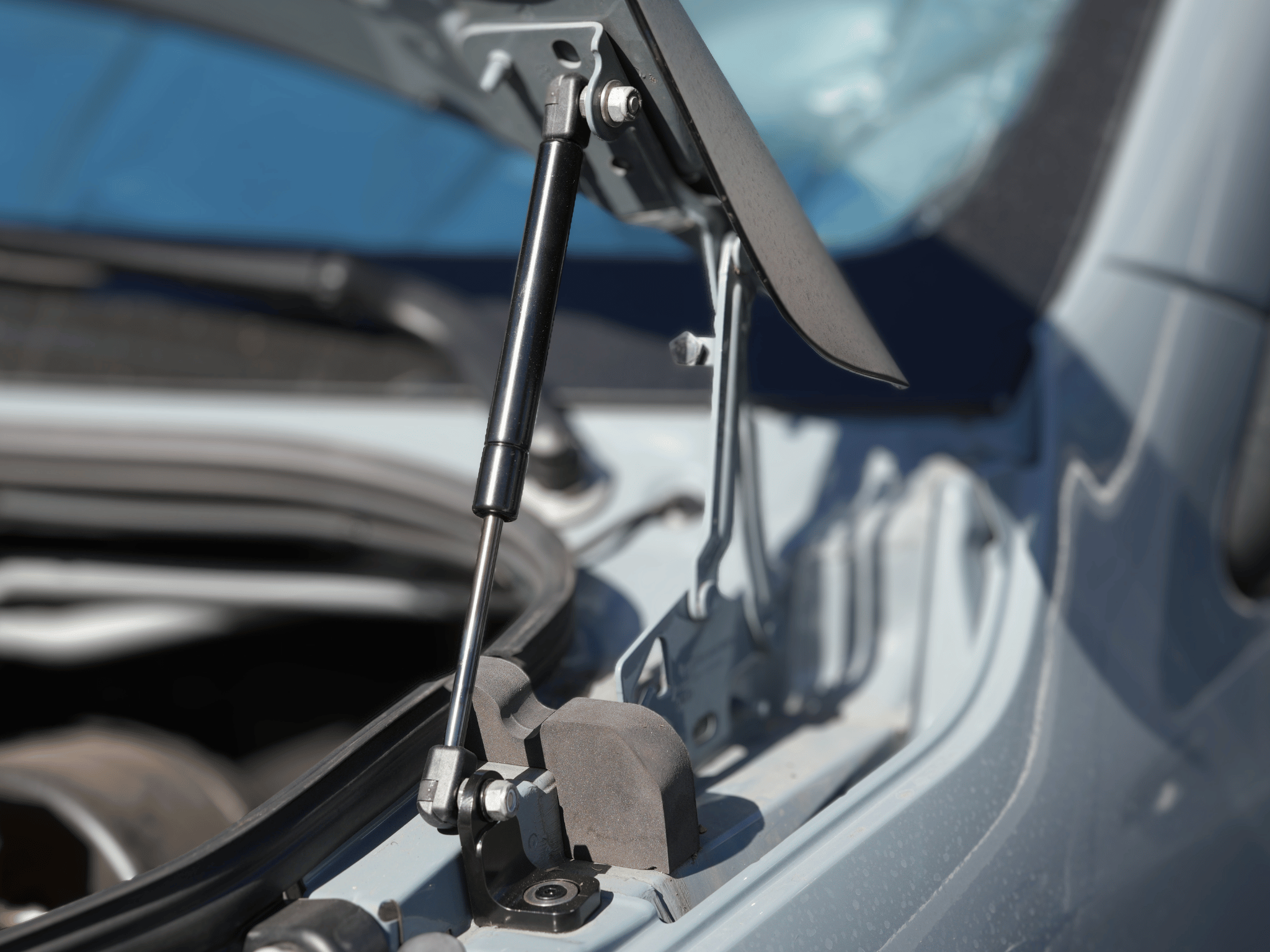 Hood strut assembly with pivot bracket holding the hood above engine bay