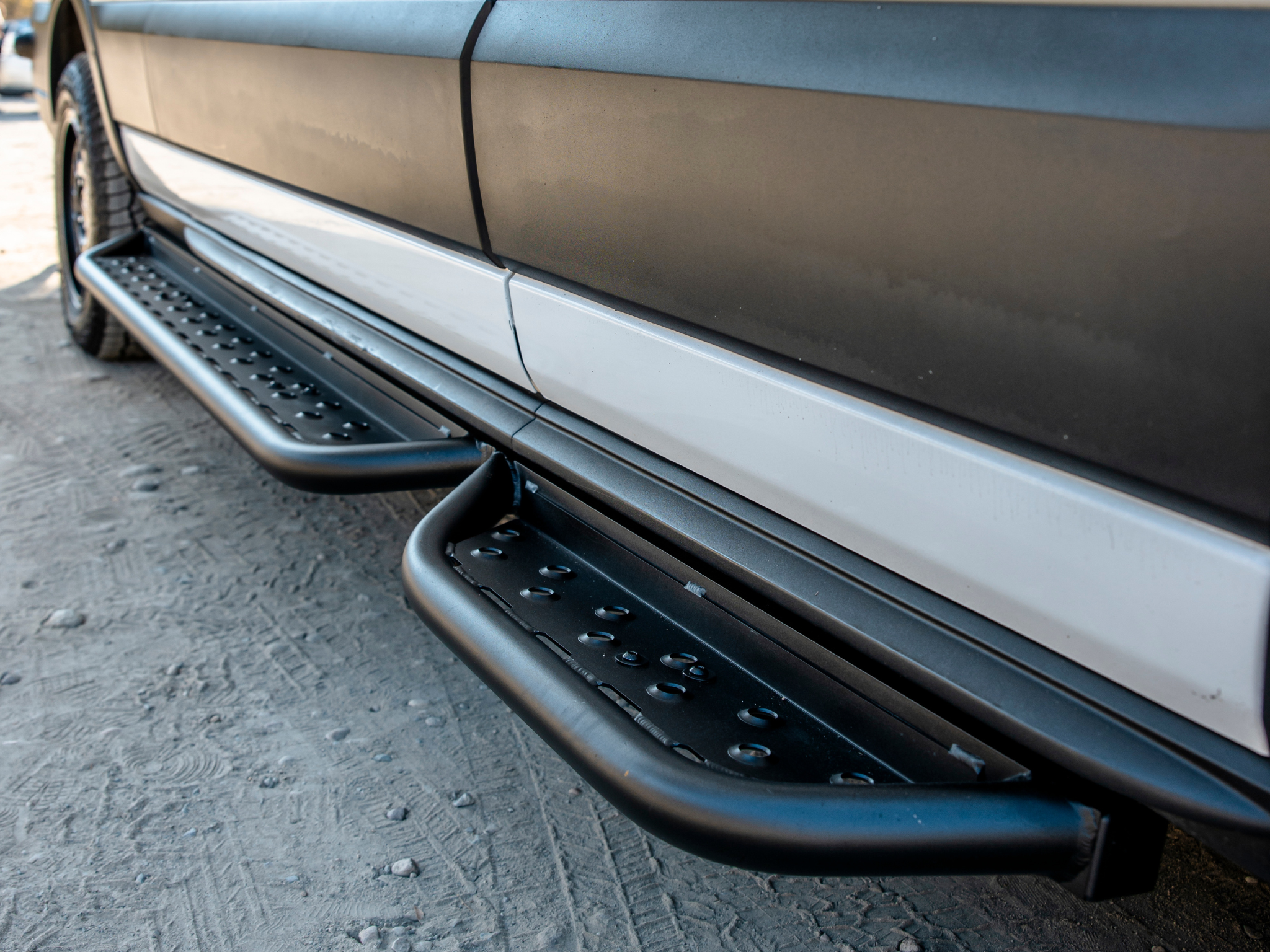 Installed black perforated side steps with anti-slip holes along the van