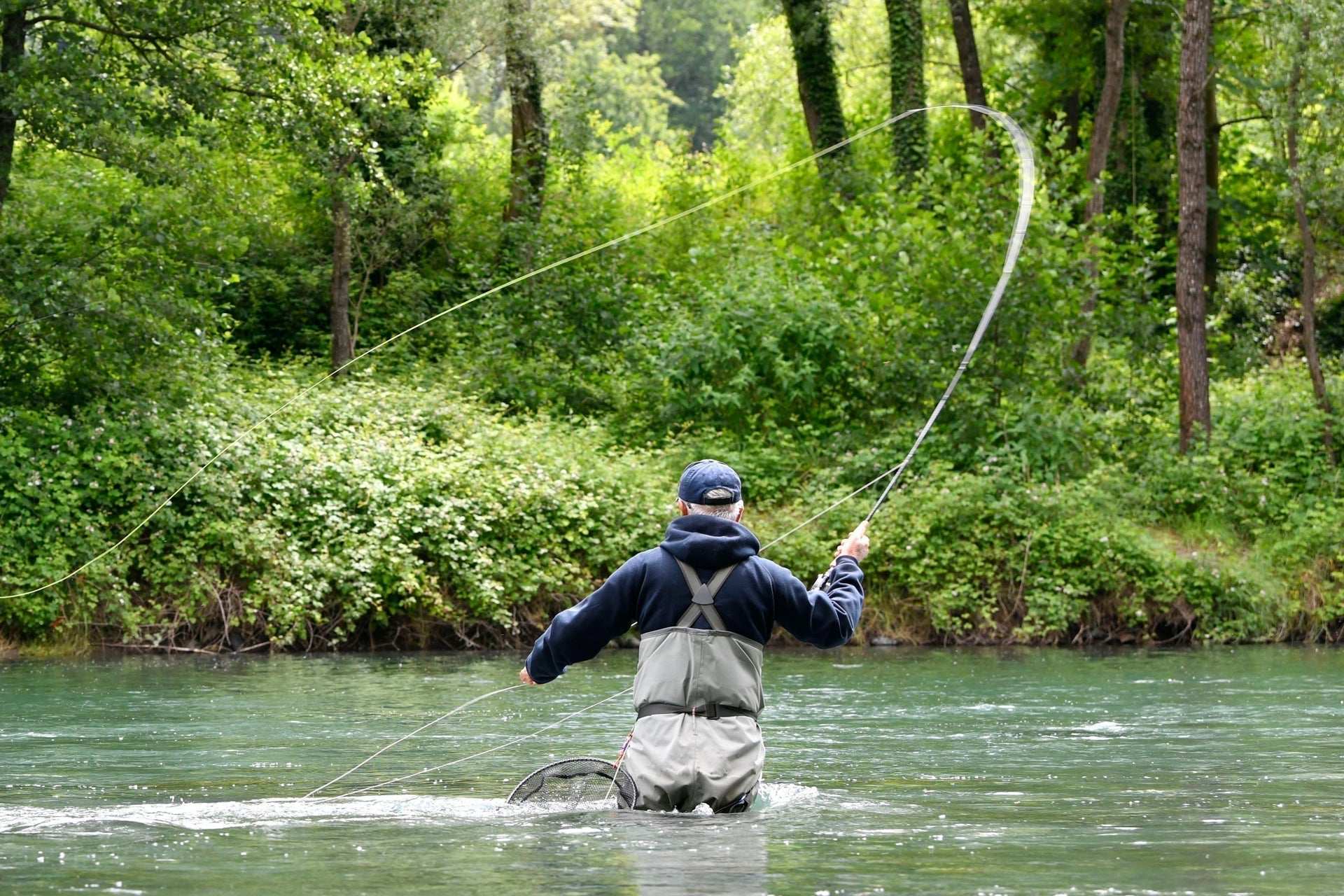 Fly fisherman casting a line on a river from a small boat