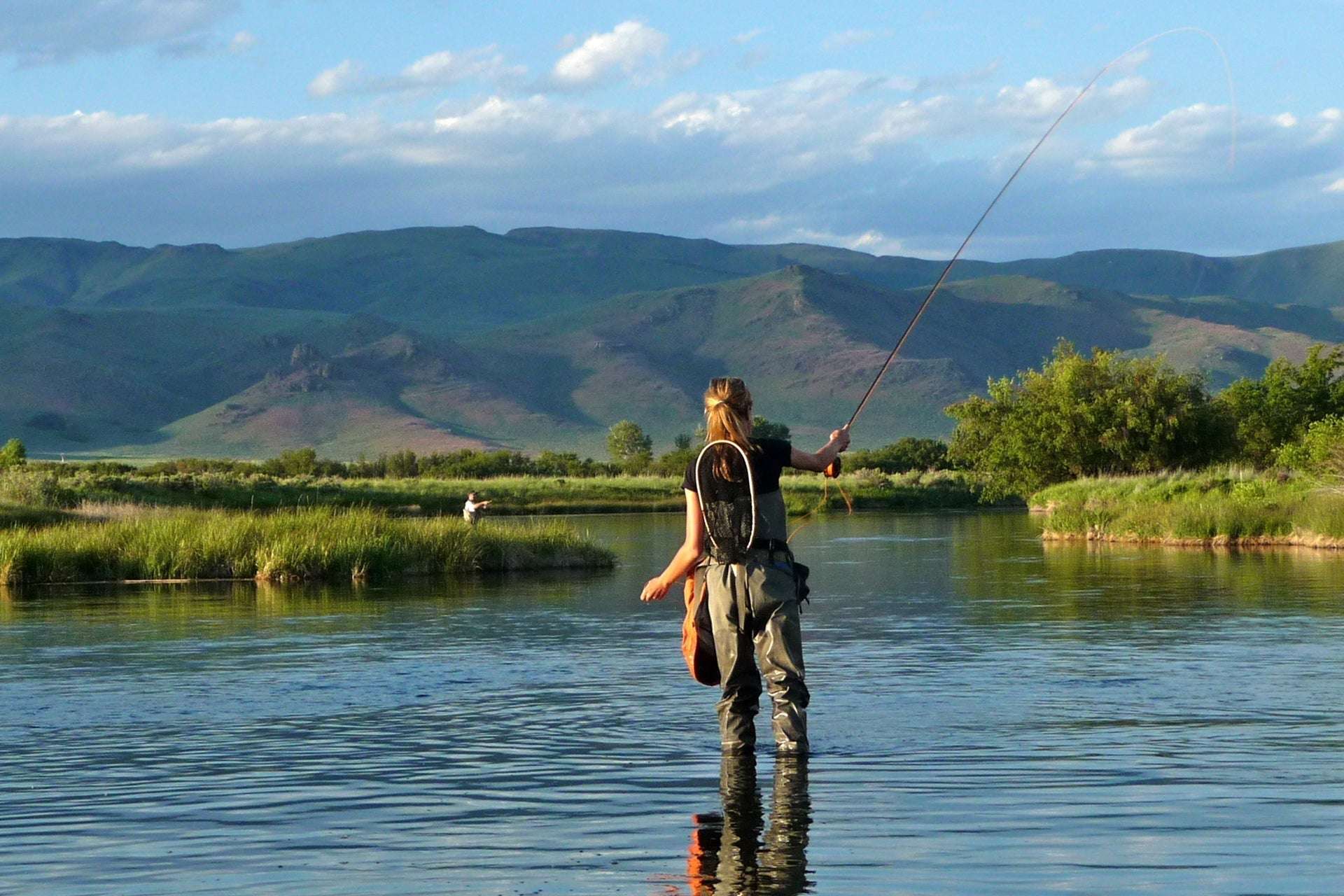 Person fishing in a lake with mountainous background, standing in water