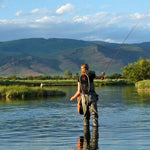 Person fishing in a lake with mountainous background, standing in water