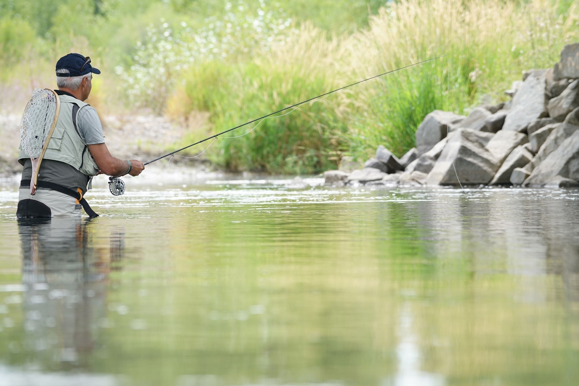 Angler casting from the riverbank with a fly fishing rod