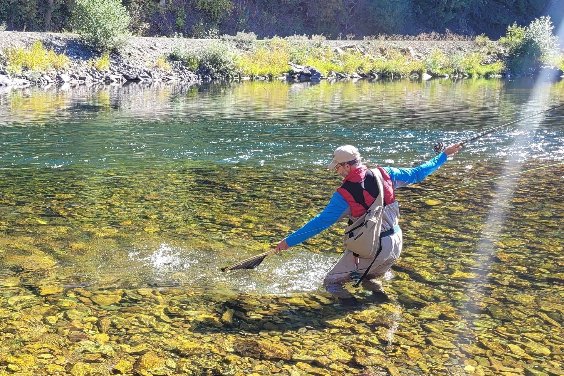 Angler wading in clear river holding a fly-fishing rod