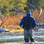 Angler fishing in shallow river, holding a fly fishing rod and line