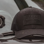 Dark trucker cap with STLHD logo patch on front panel, side view