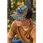 Duck-feather riverside cap worn by a person; bottomland camo with brown mesh back