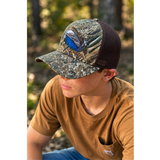 Duck-feather riverside cap worn by a person; bottomland camo with brown mesh back