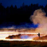 Fisherman casting a line near a misty shoreline at dusk