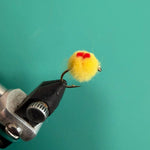 Fuzzy yellow pom-pom with red center on black metal clip attachment