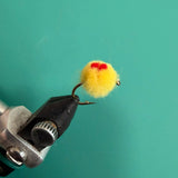 Fuzzy yellow pom-pom with red center on black metal clip attachment