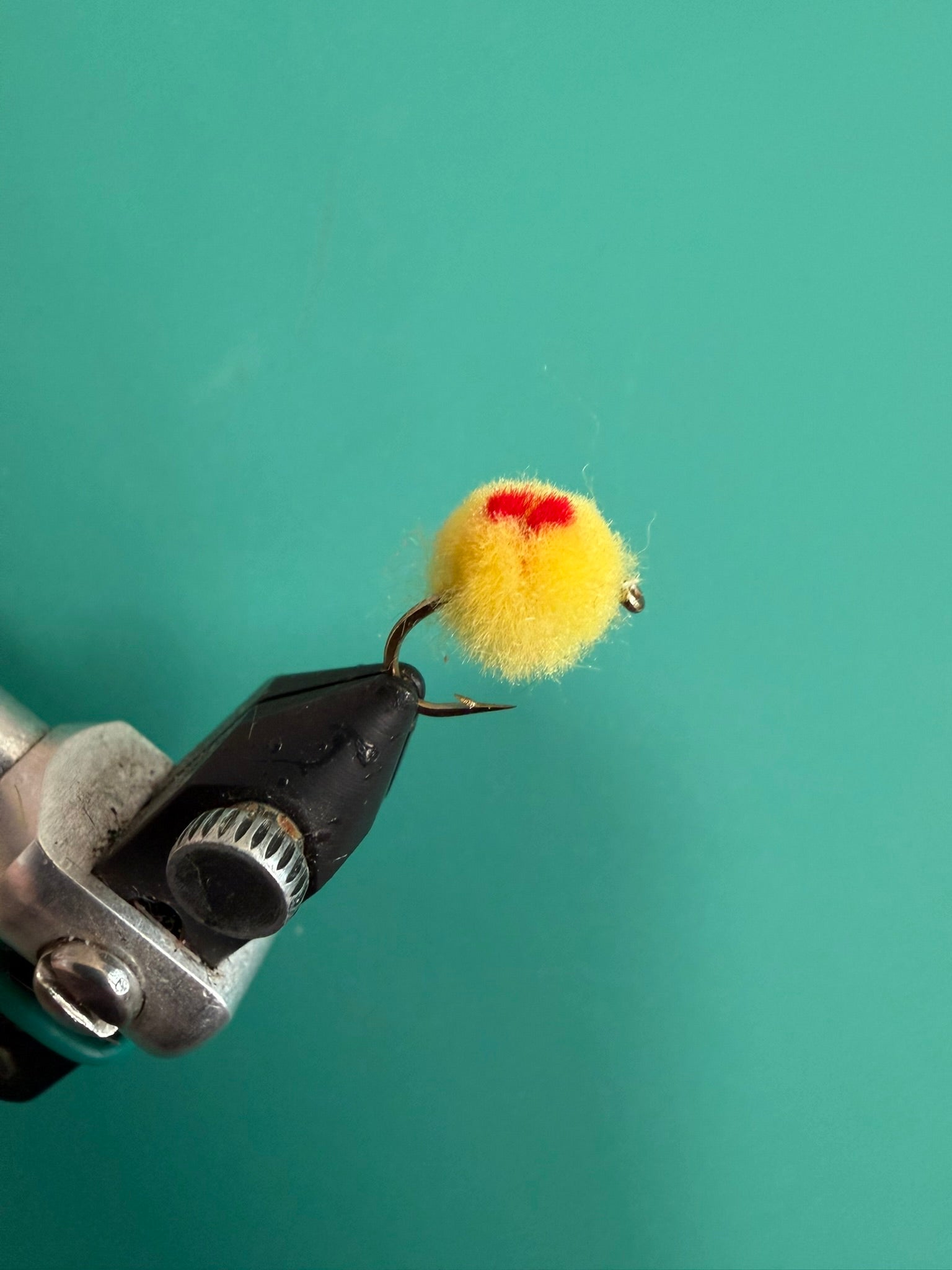 Fuzzy yellow pom-pom with red center on black metal clip attachment