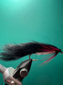 Black fishing fly with long black hair and slender tail strands on a hook