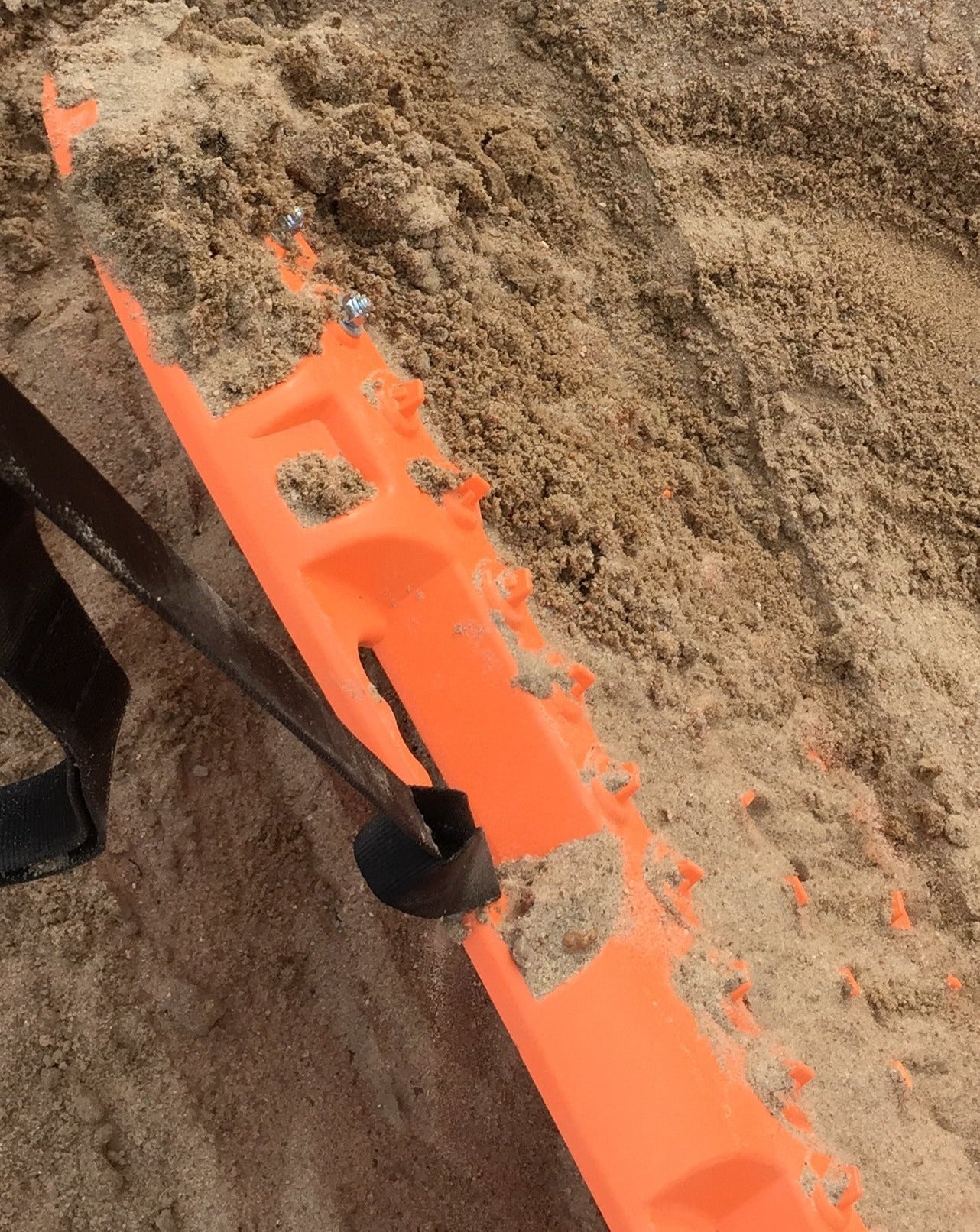 Orange recovery leash strap with black end, lying across dirt ground
