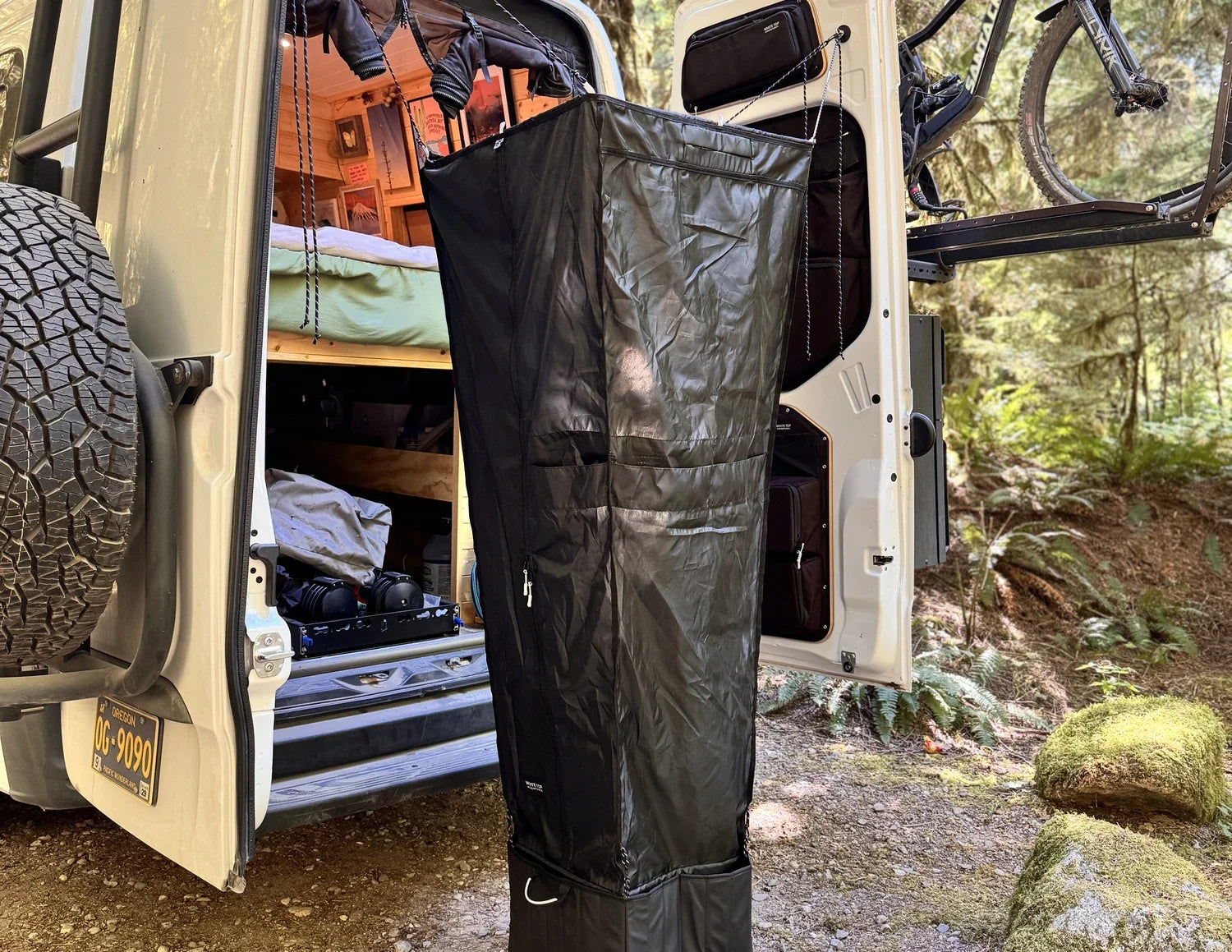 Black hanging shower bag attached to an open van door for outdoor rinsing