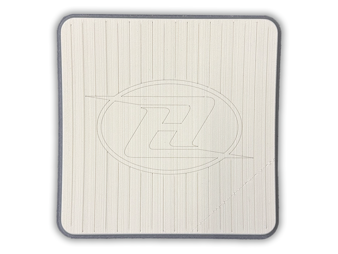 Square deck grip patch with vertical ridges and oval logo, off-white/cream with shadow.