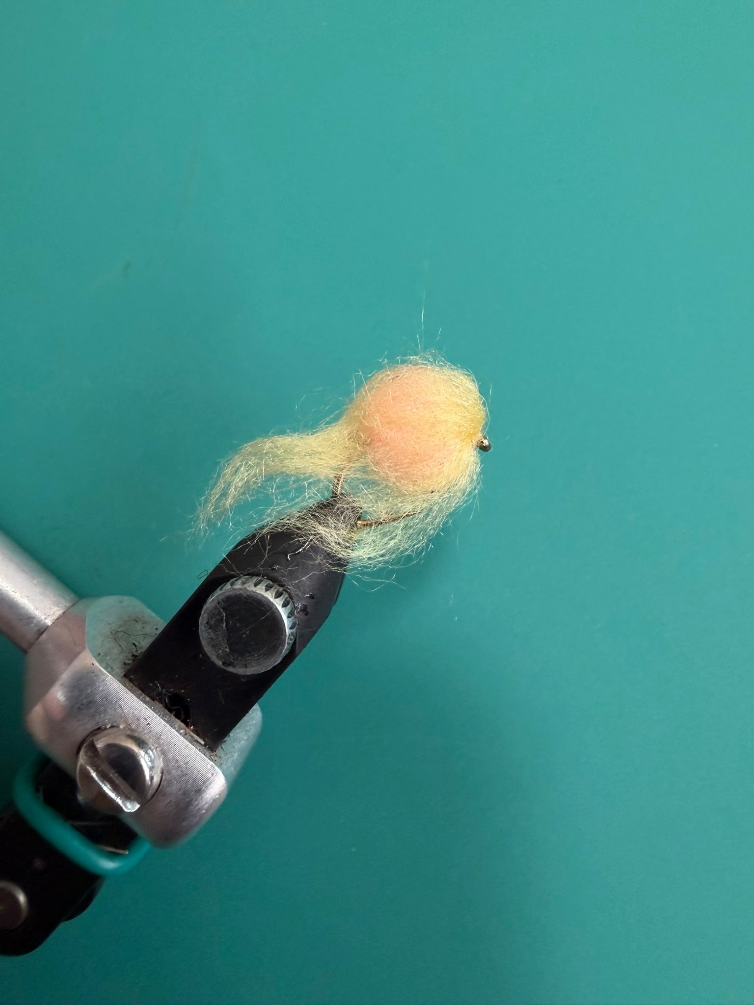 Wool-felt egg figurine in light yellow on a crafting tool clamp