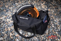 Black recovery gear bag on gravel with orange recovery hose in main compartment