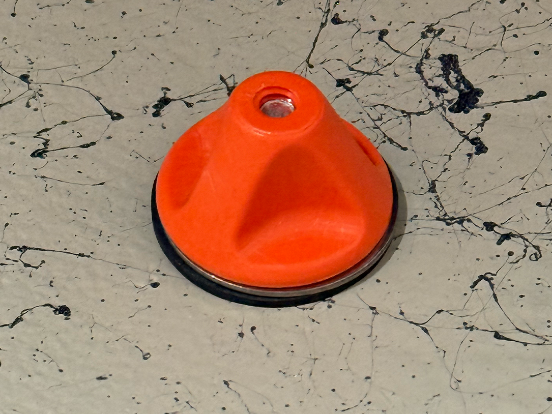 Orange drain plug cap with central hole and black rim base, top view.