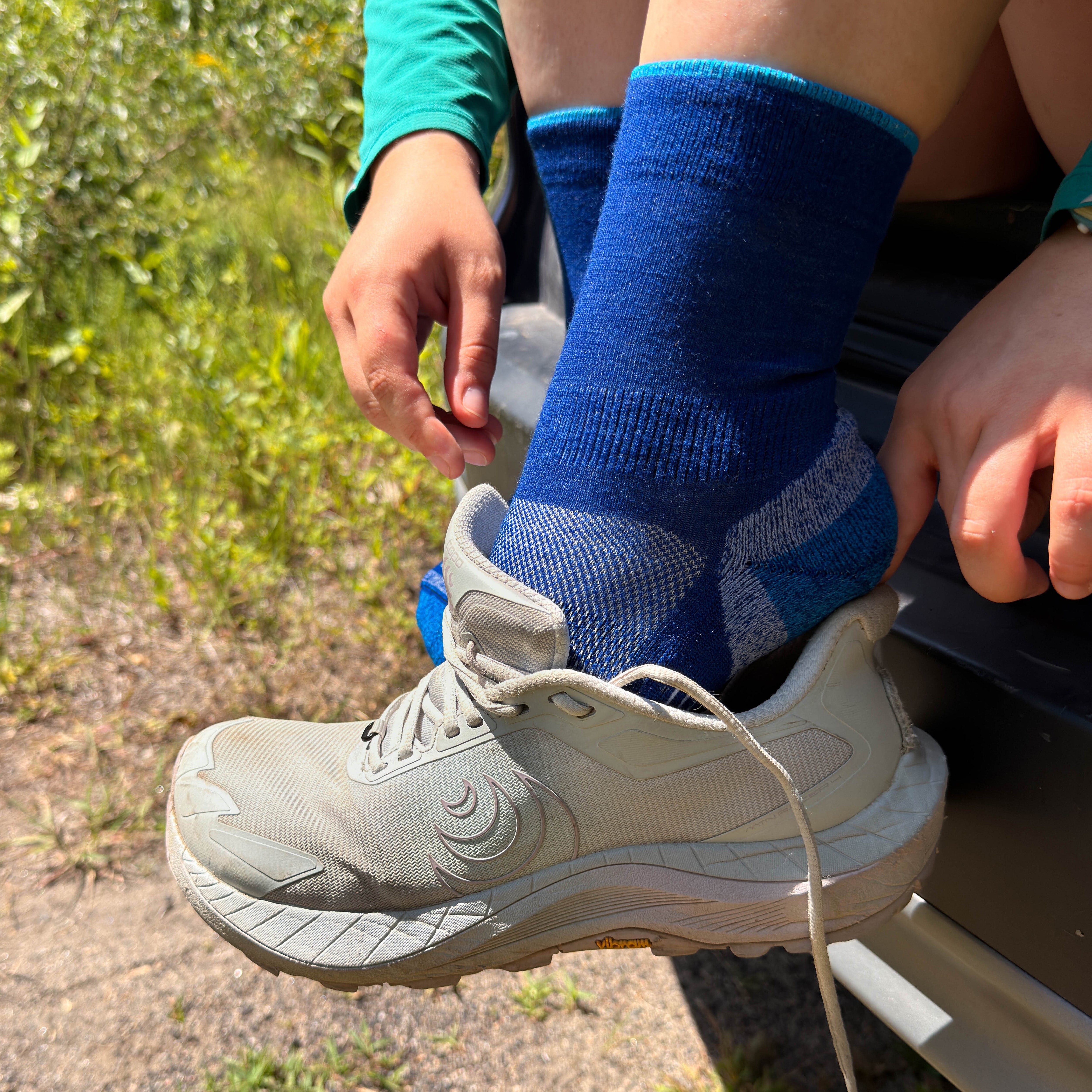 Blue mini crew running socks on foot with trail shoe visible in outdoor setting.