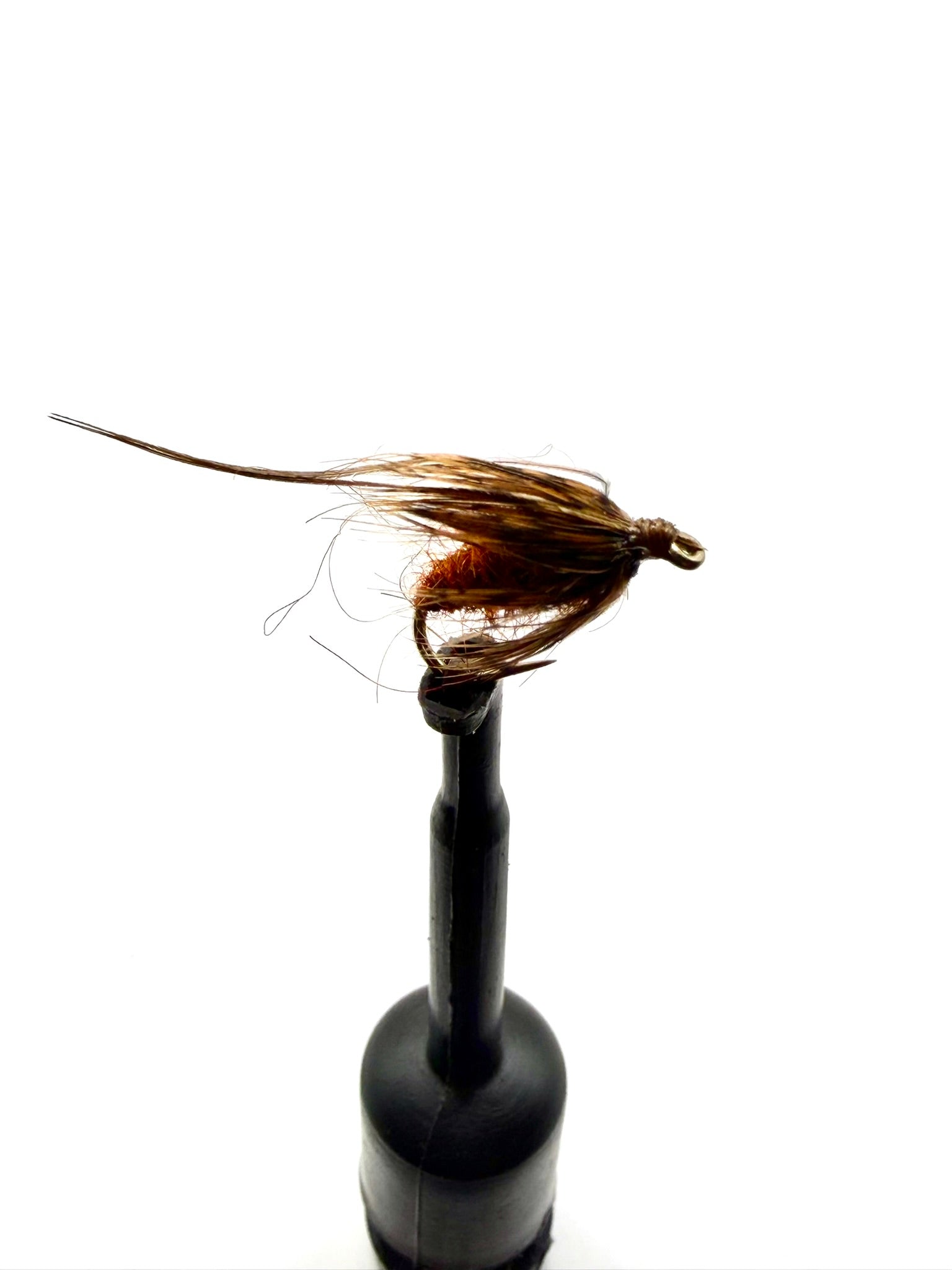 Brown-and-amber fuzzy pupa fly on hook, shown side view on black holder