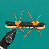 Ant-shaped decorative pin with black body, tan stripe, and orange braided legs