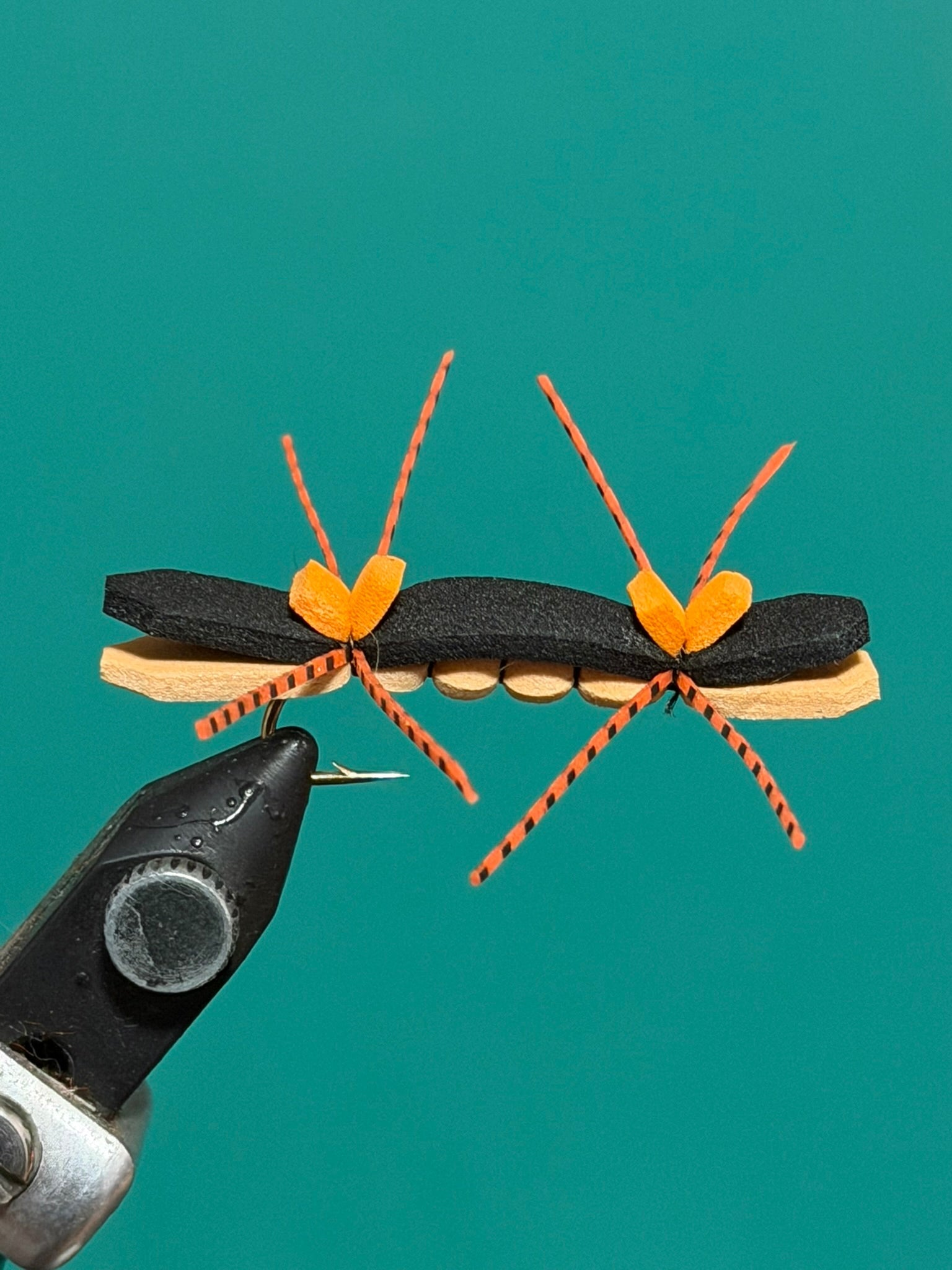 Ant-shaped decorative pin with black body, tan stripe, and orange braided legs