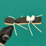 Ant-shaped decorative pin with black body, tan wings, and white leg ties